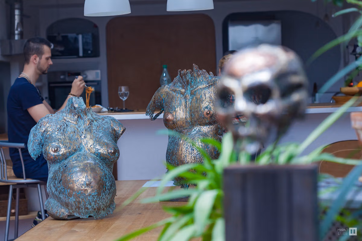 Sculptures de torses féminins en bronze patiné et crâne sur table d'un loft du Qu4tre, artiste déjeunant en arrière-plan, art et vie quotidienne mêlés à Argenteuil