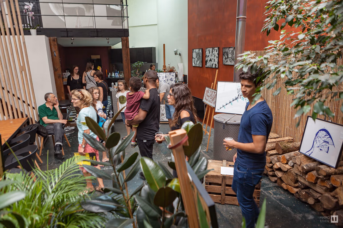 Loft végétalisé au Qu4tre avec visiteurs verre à la main, dessins graphiques sur chevalets, plantes vertes et bûches, ambiance jungle urbaine et art contemporain à Argenteuil