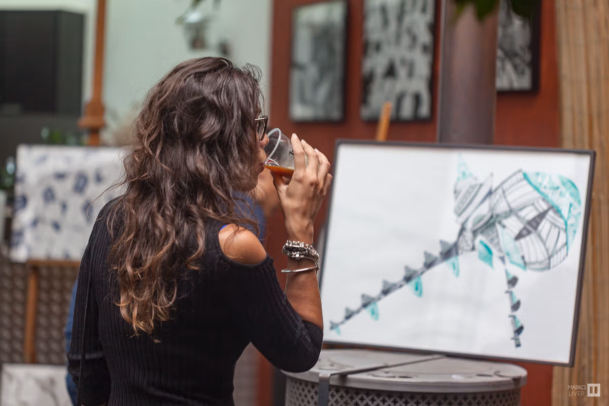 Visiteuse contemplant un dessin graphique turquoise verre à la main au Qu4tre, moment de découverte décontractée dans un atelier d'artiste, art et convivialité à Argenteuil