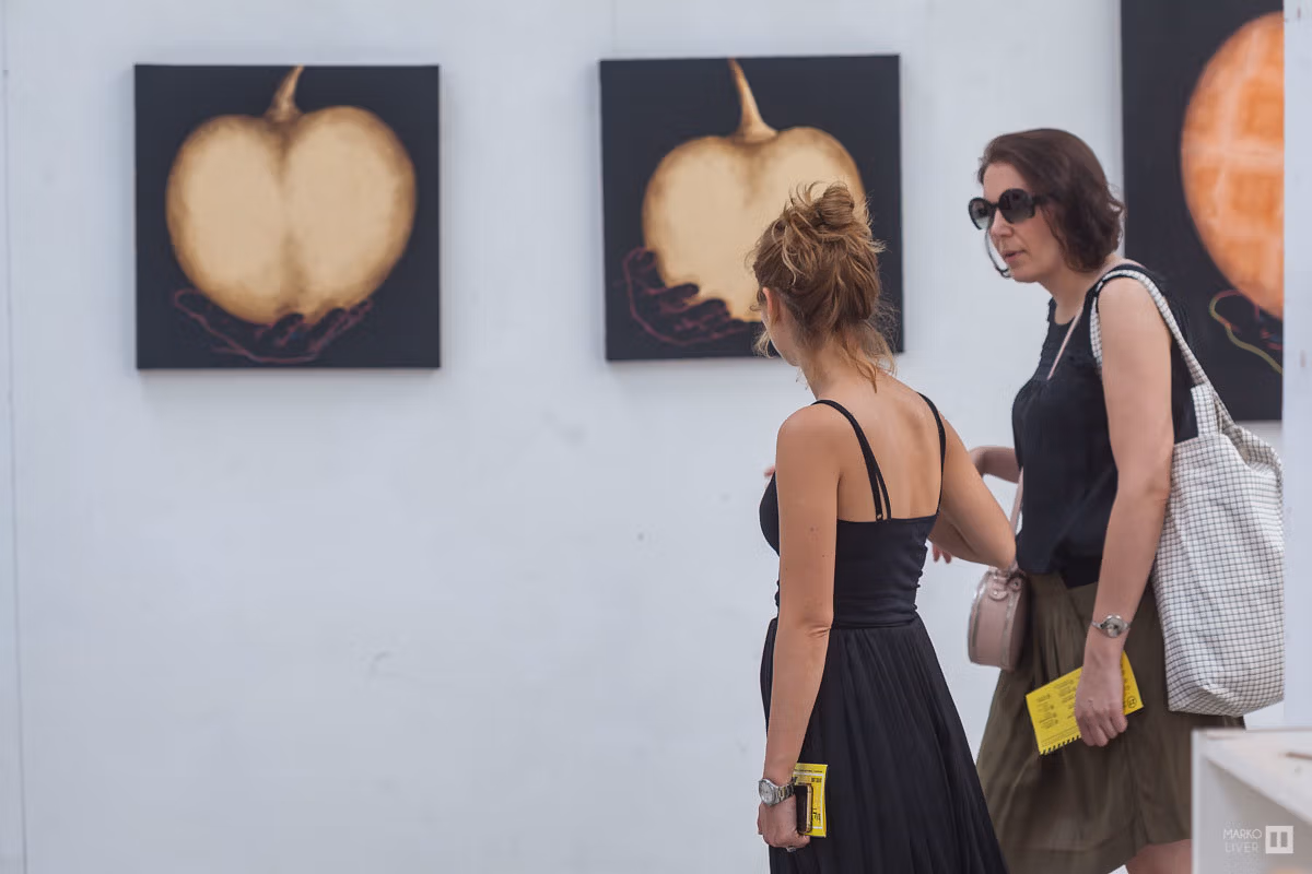 Visiteuses contemplant une série de peintures de Cat Sirot, fruits dorés sur fond noir au Qu4tre, programme en main, découverte artistique dans un atelier d'Argenteuil