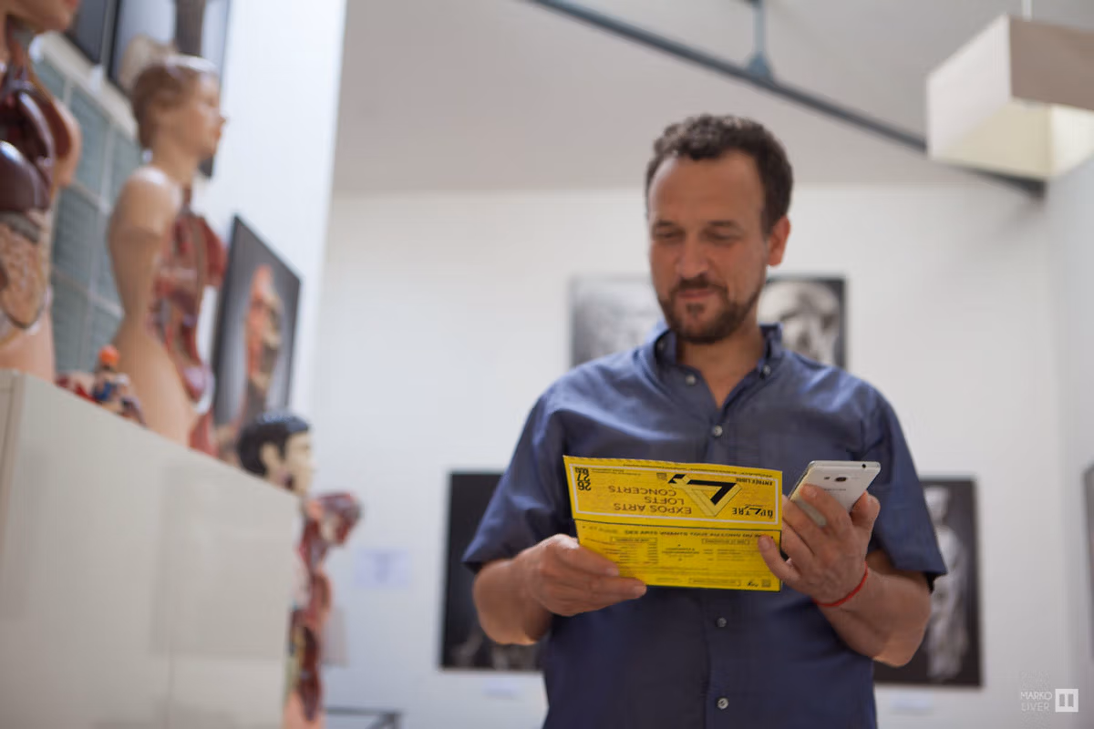 Visiteur consultant le programme au format billet de train dans un loft du Qu4tre, mannequin anatomique et photos d'art en arrière-plan, ancien entrepôt SNCF d'Argenteuil