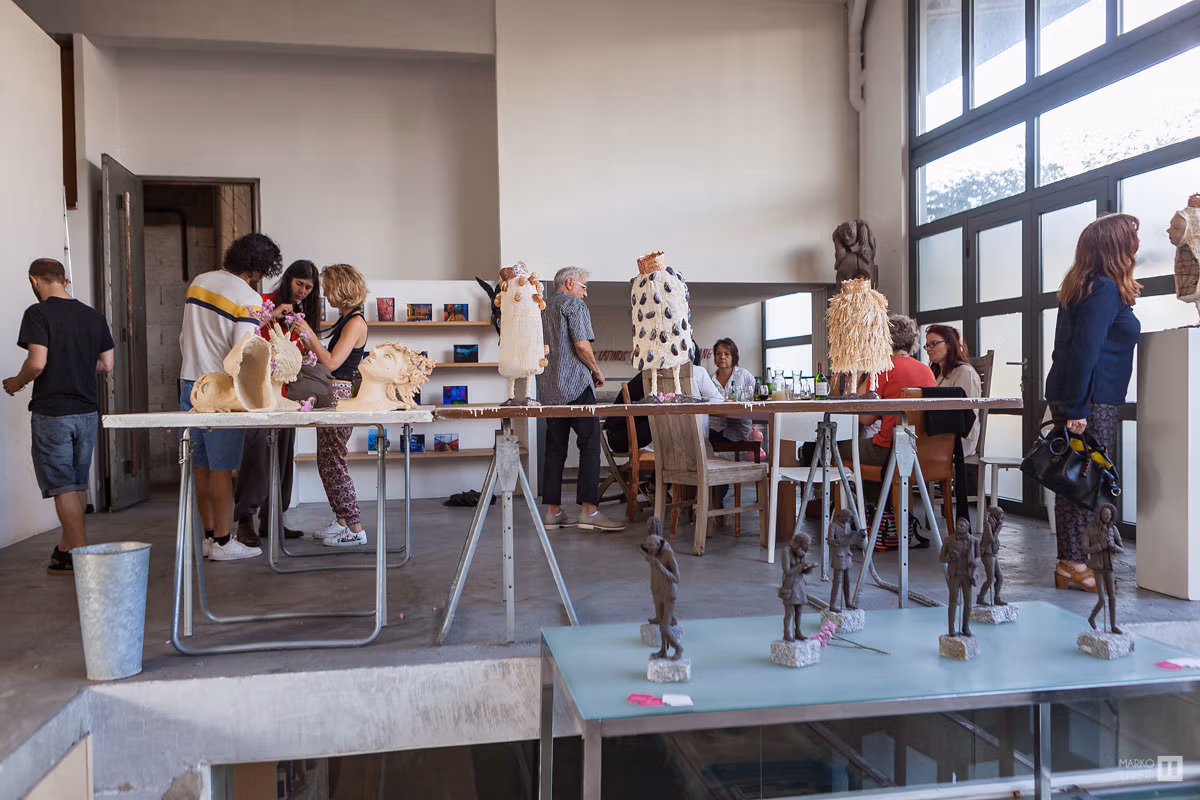 Atelier de sculpture au Qu4tre, visiteurs découvrant figurines en bronze et céramiques sur tréteaux, loft industriel avec verrière et sol béton, Argenteuil
